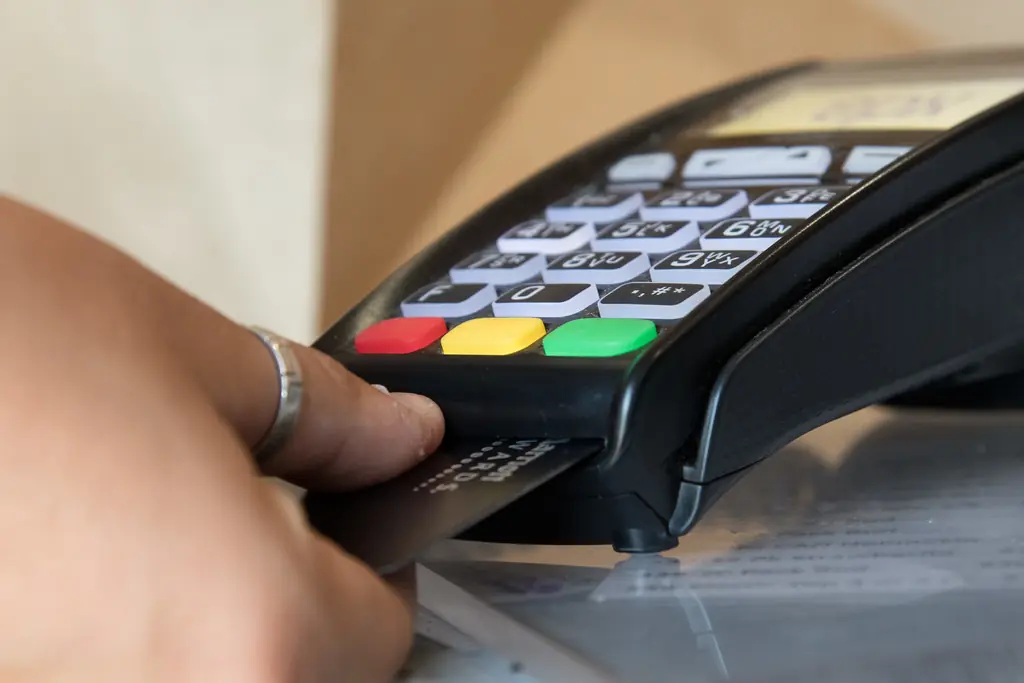 Una mano pasa una tarjeta por una terminal de pago con teclas roja, amarilla y verde.