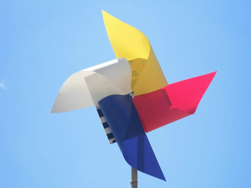 Molinete de papel con aspas amarilla, blanca, roja y azul contra un cielo azul.