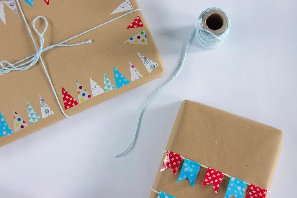 Dos paquetes envueltos en papel kraft, con pita celeste y cintas de colores, sobre una mesa blanca.