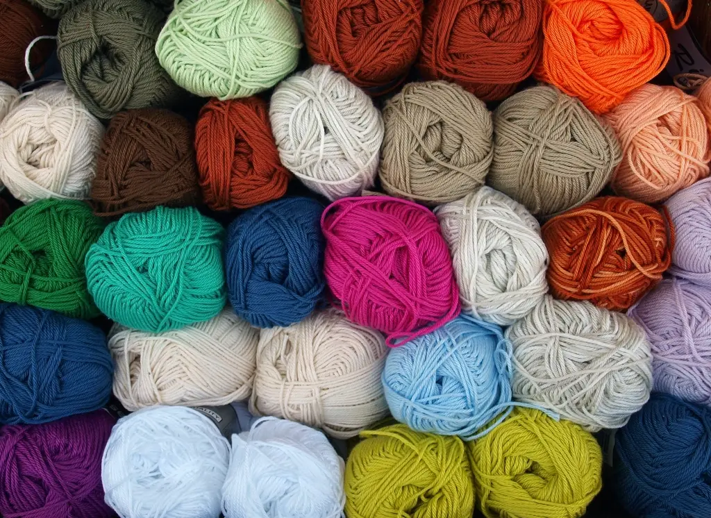 Ovillos de lana de muchos colores apilados: verdes, azules, rosados, naranjas y crudos.