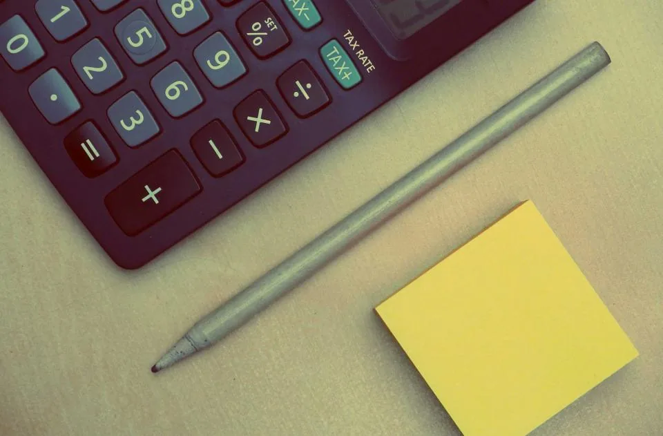 Calculadora, lápiz y un bloque de notas adhesivas amarillas sobre una mesa.
